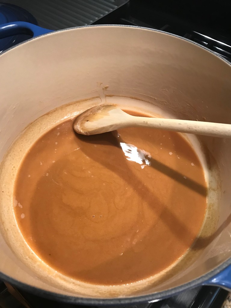 A thick, brown roux simmering in a pot with a wooden spoon resting inside, ready to be used for flavorful sauces.