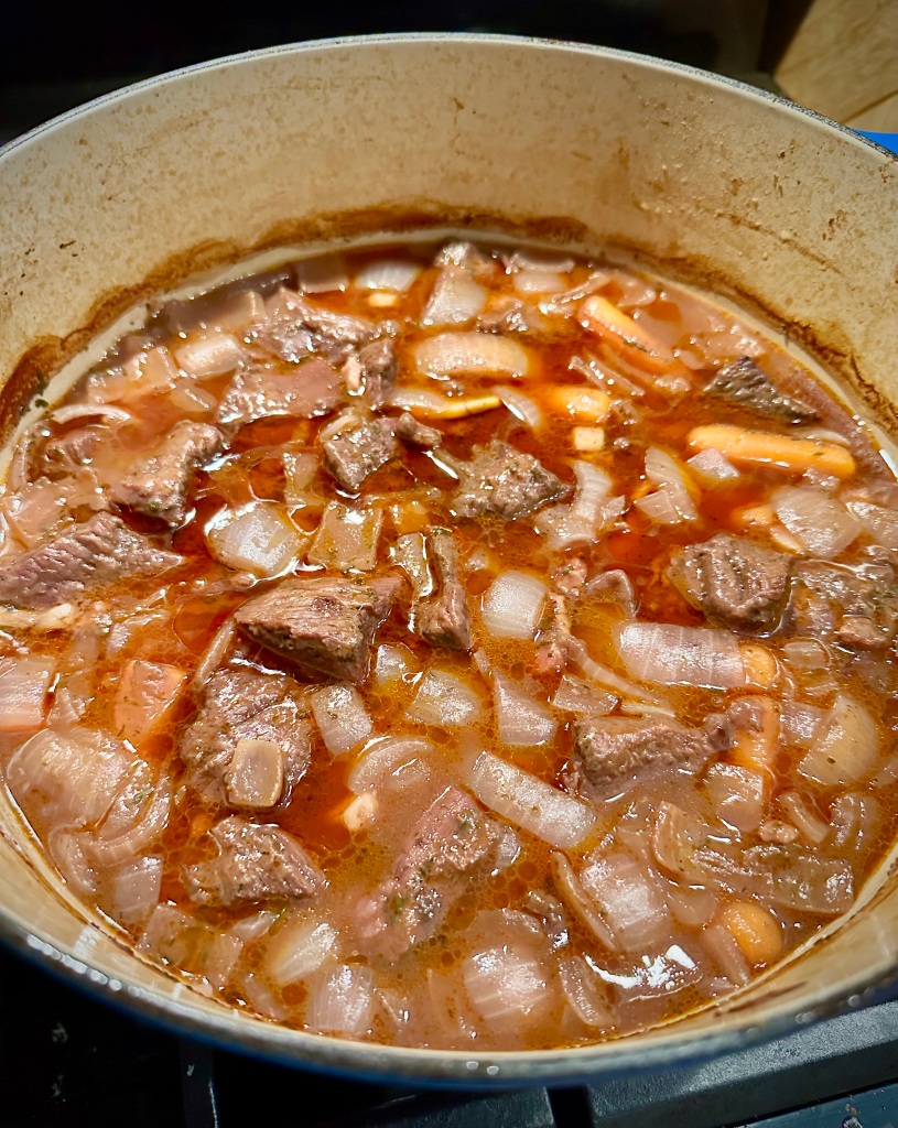 A pot of beef stew with chunks of beef, diced onions, and a rich red wine sauce.
