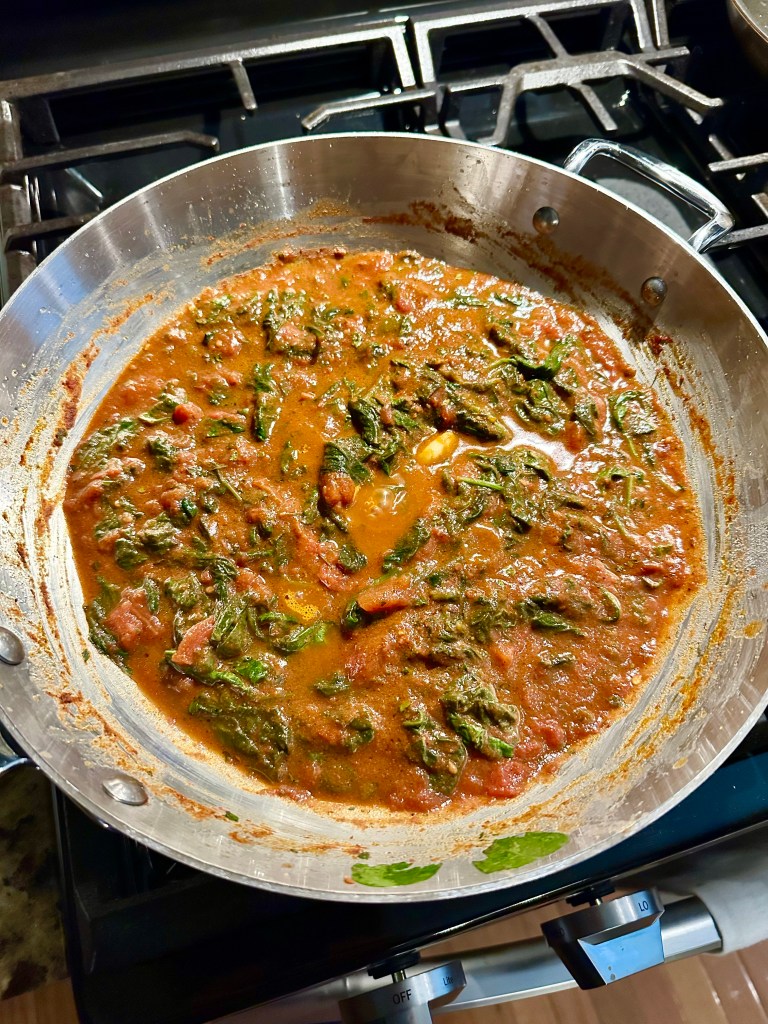 A skillet filled with a savory tomato and spinach sauce, bubbling on a stovetop.
